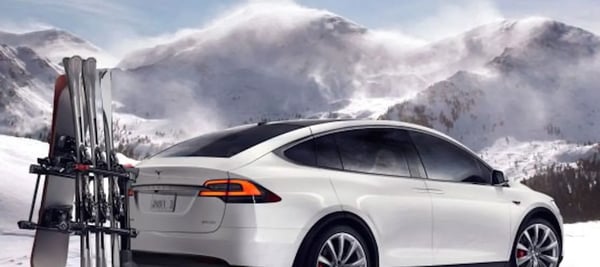 Bilde av hvit Tesla model X med ski bak på fjell