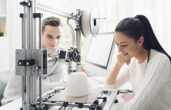 to personer som ser på en 3D-maskin som printer en krukke