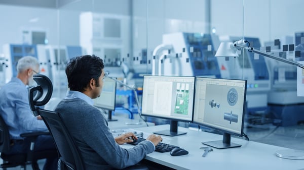 Mann som sitter foran en datamaskin med bilde av deler, på kontoret i en fabrikk. 